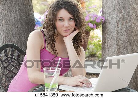 Stock Image - Pregnant woman seated at table outdoors using laptop computer, Manitoba, Canada. Fotosearch