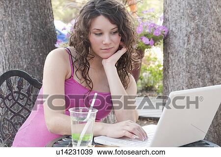 Stock Photo - Pregnant woman seated at table outdoors using laptop computer, Manitoba, Canada. Fotosearch