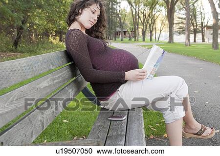 Stock Image - Pregnant woman seated on a park bench, Manitoba, Canada. Fotosearch