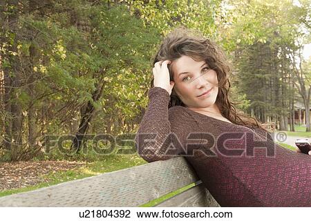 Stock Image - Pregnant woman seated on a park bench, Manitoba, Canada. Fotosearch