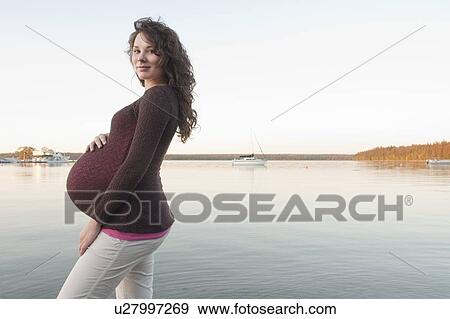 Stock Photo - Pregnant woman with hands on abdomen wading in Clear Lake, Manitoba, Canada. Fotosearch