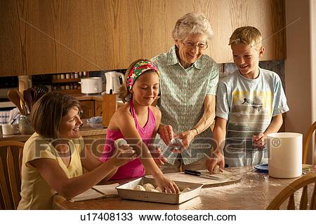 Stock Image - Senior woman, grandaughter and 2 great grandchildren preparing buns to bake; Redvers, Saskatchewan, Canada. Fotosearch
