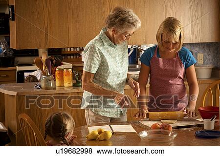 Stock Photo - Senior woman helping her great-granddaughter rolling pastry; Redvers, Saskatchewan, Canada. Fotosearch