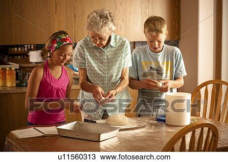 Stock Image - Senior woman preparing buns with her great grandchildren; Redvers, Saskatchewan, Canada. Fotosearch