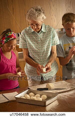 Stock Photo - Senior woman preparing buns with her great grandchildren; Redvers, Saskatchewan, Canada. Fotosearch