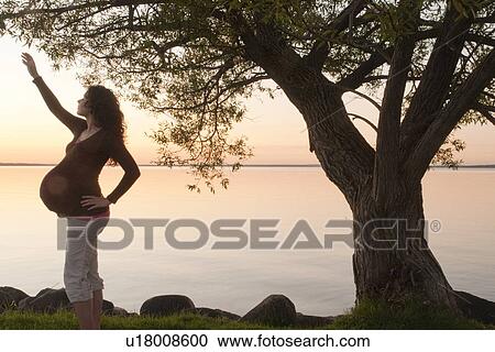 Stock Image - Silohuette of pregnant woman reaching upward, at sunset, Clear Lake, Manitoba, Canada. Fotosearch