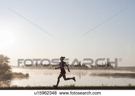Stock Photo - Silohuette of woman running by lakeshore, Clear Lake, Riding Mountain National Park, Manitoba, Canada. Fotosearch