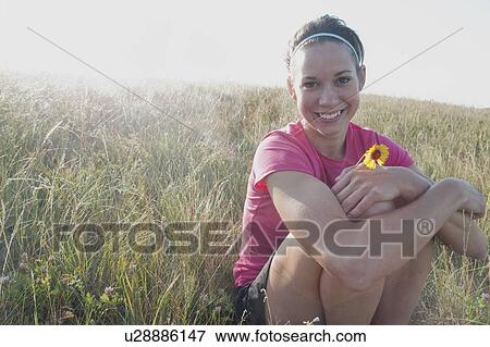 Smiling woman holding small flower on hillside, rural Manitoba, Canada View Large Photo Image Stock Photo - Smiling woman holding small flower on hillside, rural Manitoba, Canada. Fotosearch
