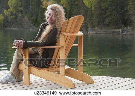 Stock Photo - Smiling woman seated in deck chair on dock, Clear Lake, Manitoba, Canada. Fotosearch