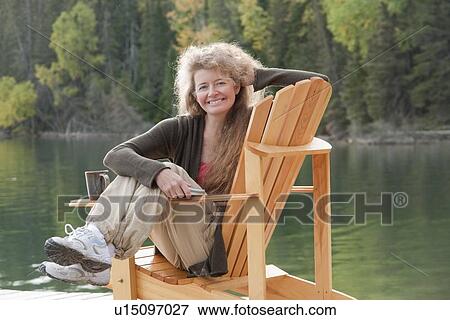 Stock Photo - Smiling woman seated sideways on deck chair on dock, Clear Lake, Manitoba, Canada. Fotosearch