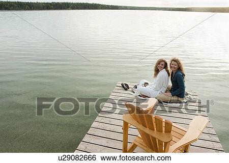Stock Photograph - Tow women seated on dock, Clear Lake, Manitoba, Canada. Fotosearch