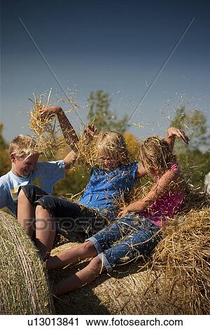 Stock Image - Tweens on bales put straw in each others hair; Redvers, Saskatchewan, Canada. Fotosearch