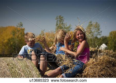Stock Image - Tweens on bales put straw in each others hair; Redvers, Saskatchewan, Canada. Fotosearch