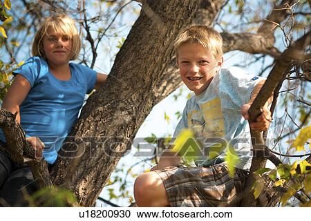 Stock Image - Twelve year old girl and twelve year old boy in tree, autumn; Redvers, Saskatchewan, Canada. Fotosearch