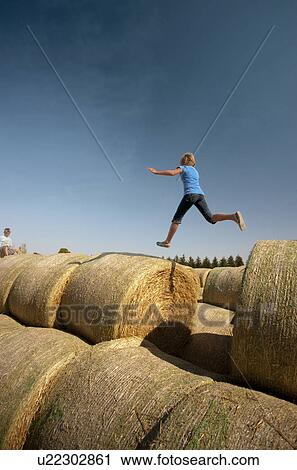 Stock Image - Twelve year old girl leaps between bales; Redvers, Saskatchewan, Canada. Fotosearch