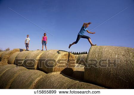 Twelve year old girl leaps between bales as 10 year old girl and 12 year old boy watch; Redvers, Saskatchewan, Canada View Large Photo Image Stock Photo - Twelve year old girl leaps between bales as 10 year old girl and 12 year old boy watch; Redvers, Saskatchewan, Canada. Fotosearch