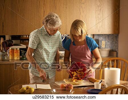 Stock Photography - Twelve year old girl pours peaches into pie shell with great grandmother beside; Redvers, Saskatchewan, Canada. Fotosearch