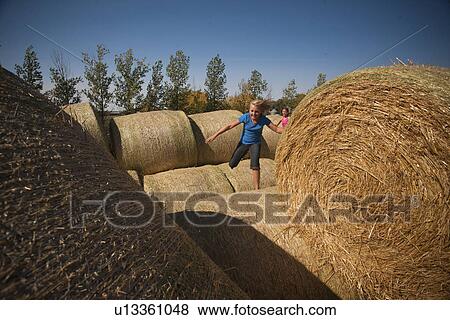 Stock Photo - Two girls running on straw bales; Redvers, Saskatchewan, Canada. Fotosearch