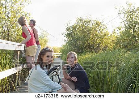 Stock Photo - Two moms and two teens pausing on boardwalk in marsh, Riding Mountain National Park, Manitoba, Canada. Fotosearch