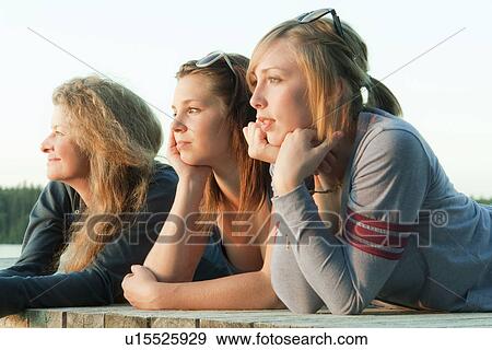Stock Photo - Two teen girls and woman in 50's lookng out over lake from dock, Riding Mountain National Park, Manitoba, Canada. Fotosearch