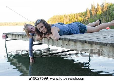 Stock Photo - Two teen girls lying on dock of Clear Lake, Riding Mountain National Park, Manitoba, Canada. Fotosearch