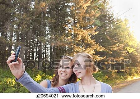 Stock Image - Two teen girls on walk taking cell phone picture on walk, Riding Mountain National Park, Manitoba, Canada. Fotosearch