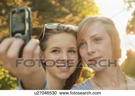 Stock Image - Two teen girls on walk taking cell phone picture on walk, Riding Mountain National Park, Manitoba, Canada. Fotosearch