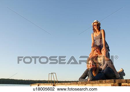Stock Image - Two teens and mom posing in pyramid on dock by lake, Riding Mountain National Park, Manitoba, Canada. Fotosearch