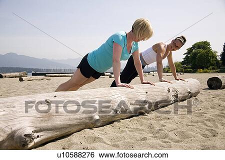 Stock Photograph - Two women doing push-ups on log at beach, Vancouver, BC. Fotosearch