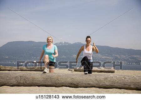 Stock Image - Two women doing step ups on log at beach, Vancouver, BC. Fotosearch