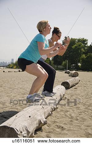 Stock Image - two women jumping onto log at beach, Vancouver, BC. Fotosearch
