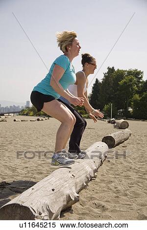 Stock Photography - two women jumping onto log at beach, Vancouver, BC. Fotosearch
