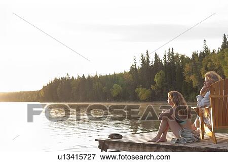 Stock Photo - Two women seated on dock at sunset, Clear Lake, Manitoba, Canada. Fotosearch