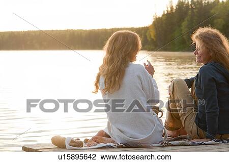 Stock Image - Two women seated on dock chatting, Clear Lake, Manitoba, Canada. Fotosearch