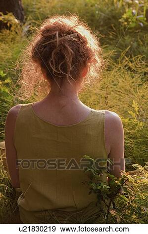 Stock Photo - View of woman from the back, seated outdoors, Clear Lake, Manitoba. Fotosearch