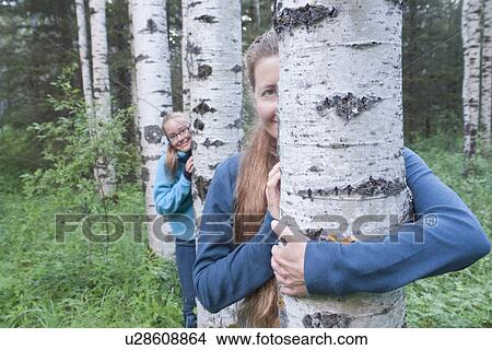 Picture - Woman and girl peeking out from behind trees in grove, Manitoba, Canada. Fotosearch