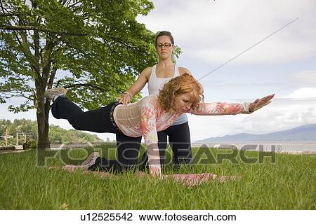 Stock Image - Woman and instructor doing yoga in park, Vancouver, BC. Fotosearch
