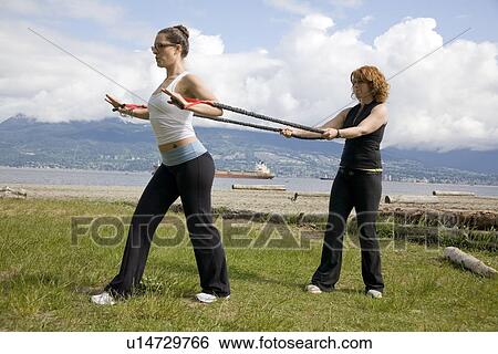 Stock Photograph - Woman and instructor using yoga bands on beach, Vancouver, BC. Fotosearch