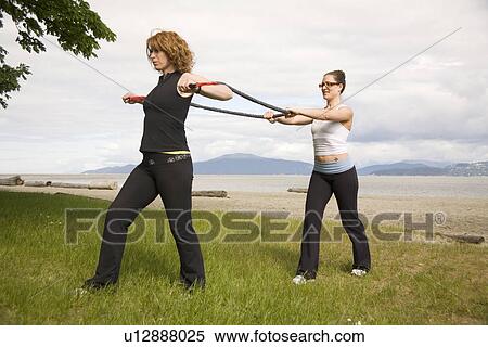 Stock Photography - Woman and instructor using yoga bands on beach, Vancouver, BC. Fotosearch