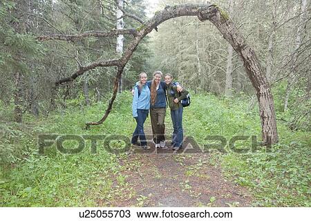 Stock Image - Woman and two girls on hiking trail beside tree arched over trail, Manitoba, Canada. Fotosearch