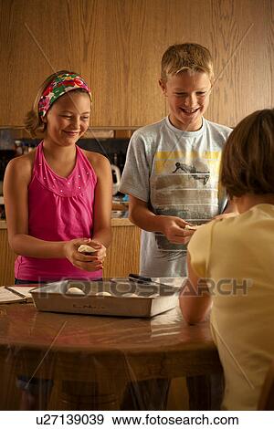Woman (back to camera) and two children (ten and twelve) preparing buns for baking; Redvers, Saskatchewan, Canada View Large Photo Image Stock Photo - Woman (back to camera) and two children (ten and twelve) preparing buns for baking; Redvers, Saskatchewan, Canada. Fotosearch