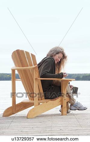 Stock Photo - Woman dialing on cellphone, seated in deck chair on dock, Clear Lake, Manitoba, Canada. Fotosearch