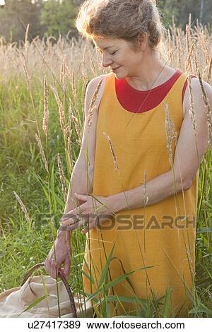 Stock Photo - Woman holding basket stands in tall grass, Manitoba, Canada. Fotosearch