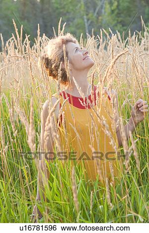 Stock Photograph - Woman holding basket stands in tall grass, Manitoba, Canada. Fotosearch