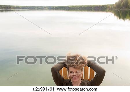 Stock Image - Woman holding up hari, seated in deck chair by Clear Lake, Manitoba, Canada. Fotosearch