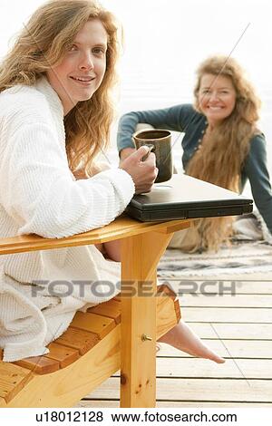 Stock Photo - Woman in deck chair smiling at camera, second woman seated on dock, Clear Lake, Manitoba, Canada. Fotosearch