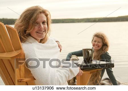 Woman in deck chair smiling at camera, second woman seated on dock, Clear Lake, Manitoba, Canada View Large Photo Image Stock Photograph - Woman in deck chair smiling at camera, second woman seated on dock, Clear Lake, Manitoba, Canada. Fotosearch