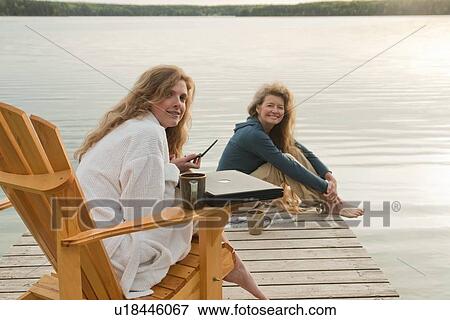 Stock Photo - Woman in deck chair using cell phone, second woman seated on dock, Clear Lake, Manitoba, Canada. Fotosearch