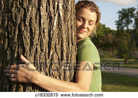 Stock Photo - Woman in her 40's hugs tree in park, Winnipeg, Canada. Fotosearch