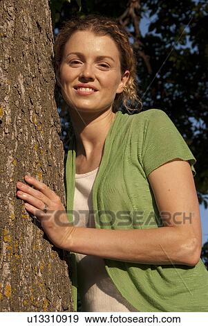 Stock Photo - Woman in her 40's leans against tree in park, Winnipeg, Canada. Fotosearch